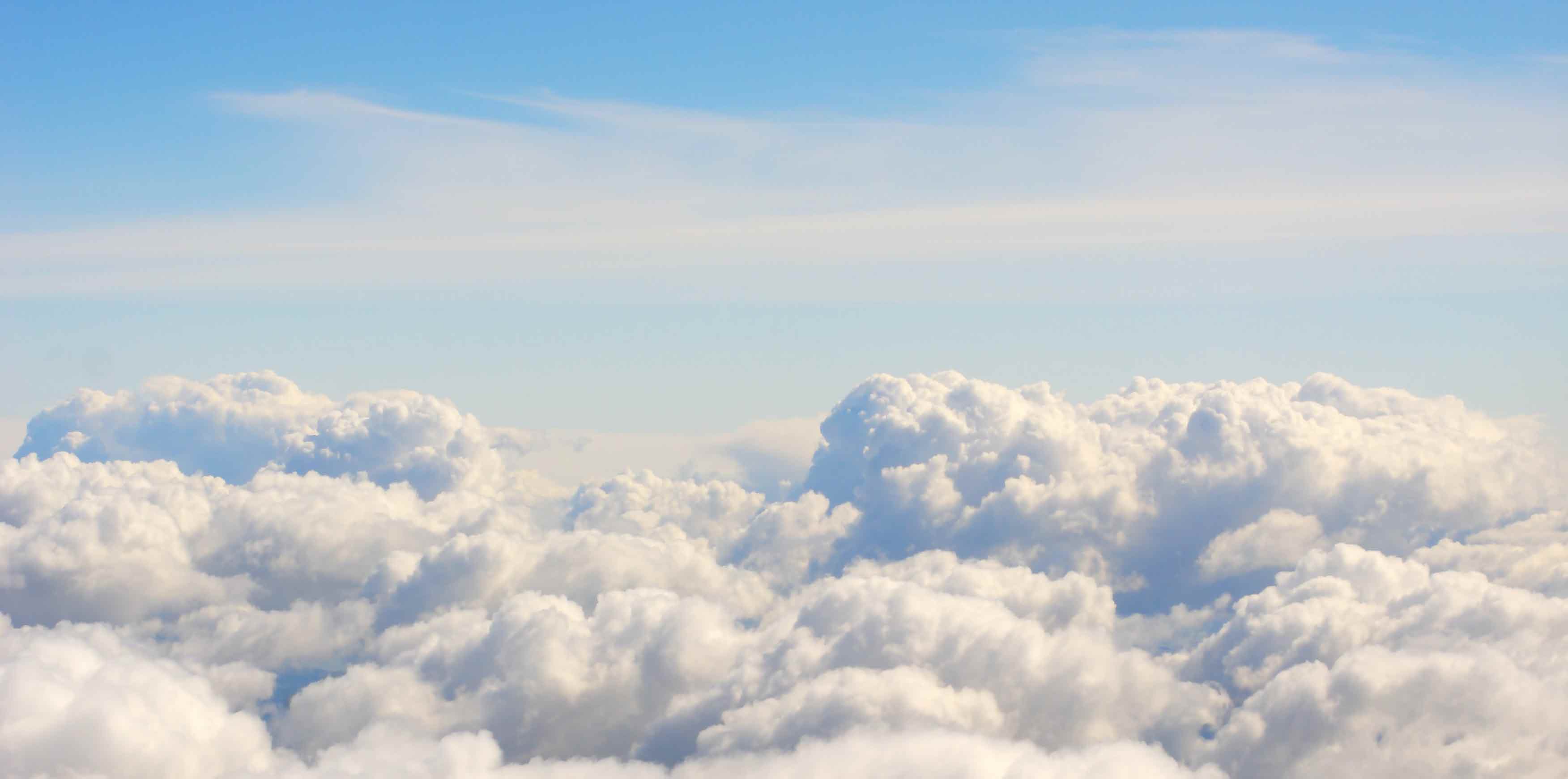 Betrachter schaut auf dicke, helle Wolkendecke herab. Darüber blauer Himmel und leicht transparente, weiter entfernte Wolken.